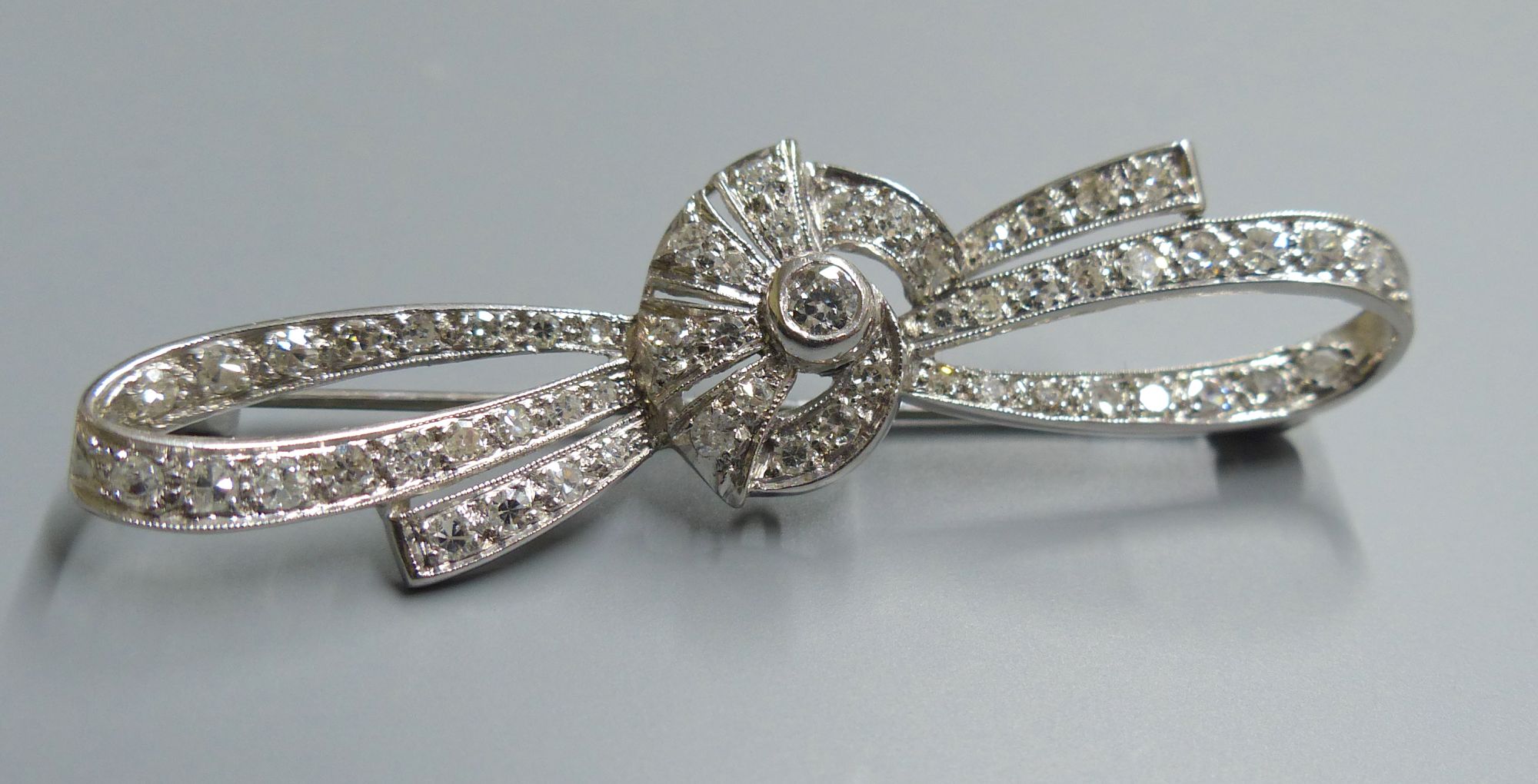 A white metal and millegrain set diamond cluster ribbon bow brooch, 54mm, gross 5.9 grams.